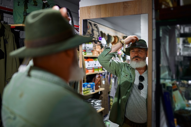 Cazador masculino barbudo eligiendo sombrero en la tienda de armas