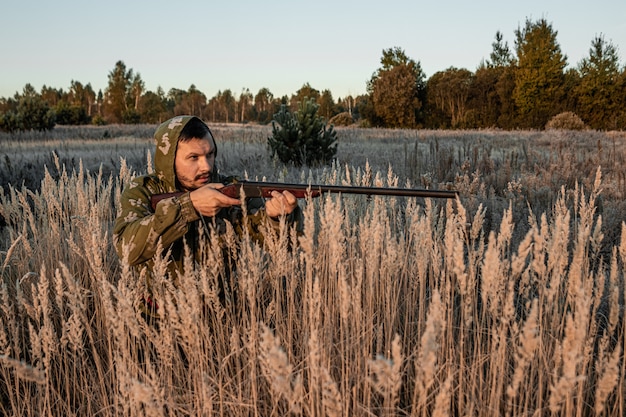 Cazador con una pistola está sentado en la hierba esperando presa