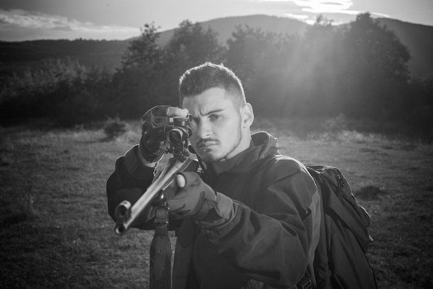 Cazador con rifle potente con alcance para detectar animales. Cazador de rifles silueteado en una hermosa puesta de sol. Temporada de caza de otoño.