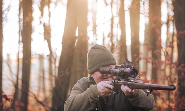 Cazador de temporada de caza de otoño con rifle buscando algún animal salvaje en un concepto de deportes al aire libre de madera o bosque