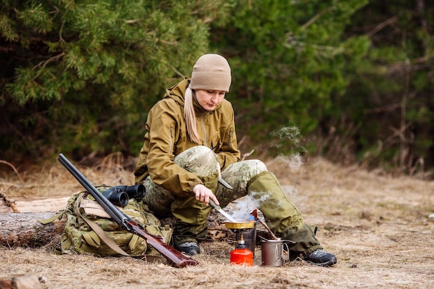 Cazadora preparando comida con un quemador de gas portátil en un bosque de invierno