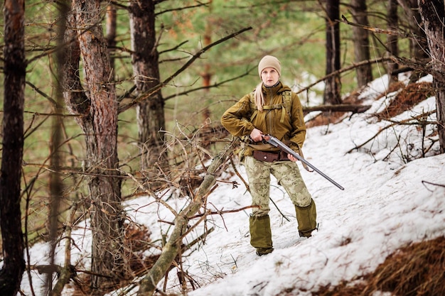 Cazadora con ropa de camuflaje lista para cazar sosteniendo un arma y caminando en el bosque