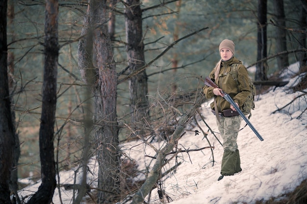 Cazadora con ropa de camuflaje lista para cazar sosteniendo un arma y caminando en el bosque