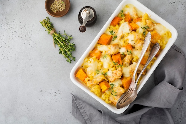 Cazuela de carne de pollo, calabaza, pasta, tomillo, queso y salsa bechamel en forma de cerámica sobre una mesa de hormigón ligero o piedra. Enfoque selectivo. Vista superior. Copie el espacio.