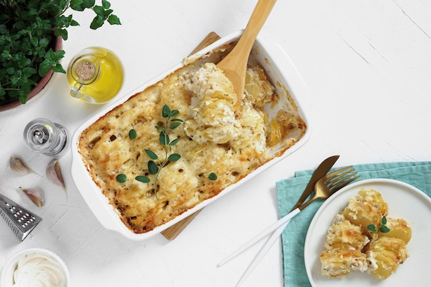 Cazuela Cocina francesa Patata casera gratinada en una sartén de cerámica para hornear Con hojas de orégano fresco aceite de oliva ajo y plato de porción Vista superior espacio de copia