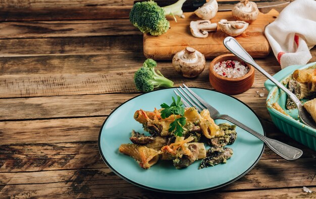 Cazuela con pasta, champiñones, salsa de brócoli y queso sobre un fondo de madera rústica