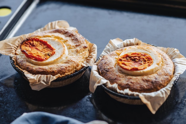 Cazuela con queso y tomate Dos raciones de cazuelas redondas en una bandeja para horno