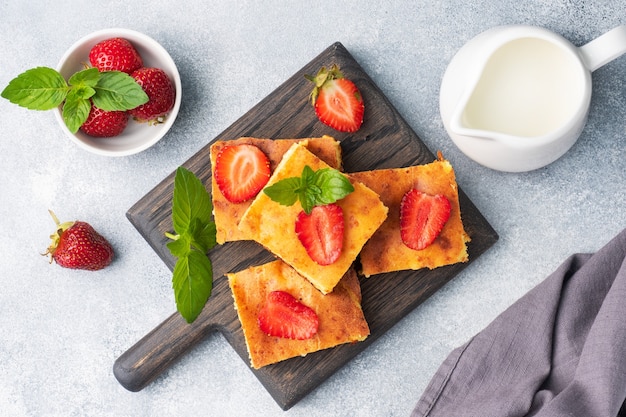 Cazuela de requesón con fresas y menta. Delicioso postre casero a base de cuajada y bayas frescas con nata. Fondo de hormigón gris de cerca.