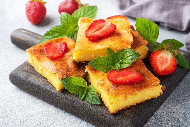 Cazuela de requesón con fresas y menta. Delicioso postre casero a base de cuajada y bayas frescas con nata. Fondo de hormigón gris de cerca.