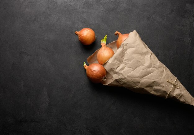 Cebola marrom fresca em um saco de papel em uma vista de mesa preta