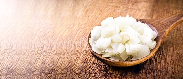 Cebola picada e alho na colher de pau, usada em cozinha rústica, ingrediente de tempero.