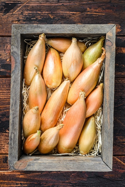 Cebolas de chalota frescas cruas Bulbos em uma caixa de madeira do mercado. Fundo de madeira escuro. Vista do topo.