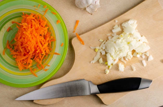 Cebolla picada en una tabla de cortar de madera y zanahoria rallada en el plato y el cuchillo