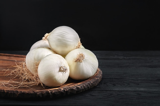 Cebollas blancas sobre una tabla de madera sobre mesa negra. alimentos orgánicos