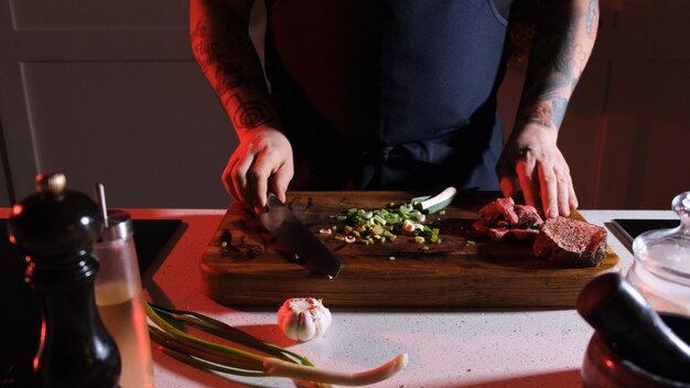 cebollas frescas picadas finamente y pedazos de carne cocida picada en una tabla de madera frente al cocinero