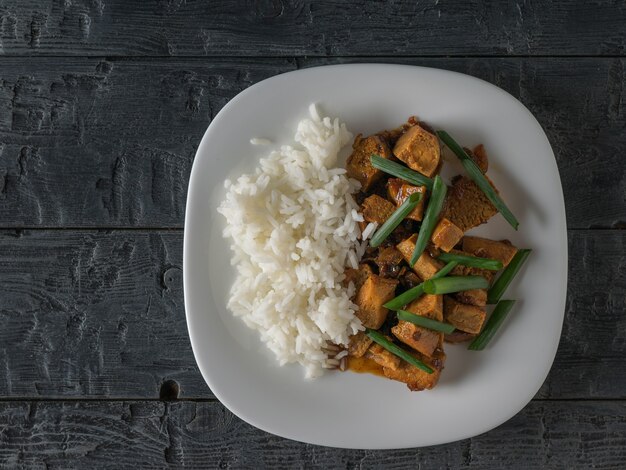 Cebollas verdes con queso tofu frito y arroz en una mesa de madera. Endecha plana. Plato asiático vegetariano.