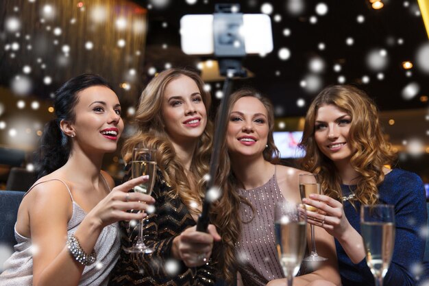 celebração, amigos, despedida de solteira, conceito de tecnologia e feriados - mulheres felizes com champanhe e bastão de selfie de smartphone tirando fotos na boate