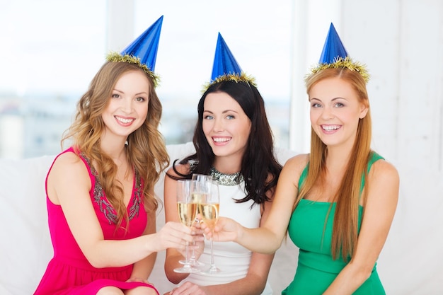 celebração, bebidas, amigos, despedida de solteira, conceito de aniversário - três mulheres sorridentes usando chapéus azuis com taças de champanhe