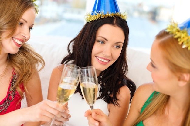 celebração, bebidas, amigos, despedida de solteira, conceito de aniversário - três mulheres sorridentes usando chapéus azuis com taças de champanhe