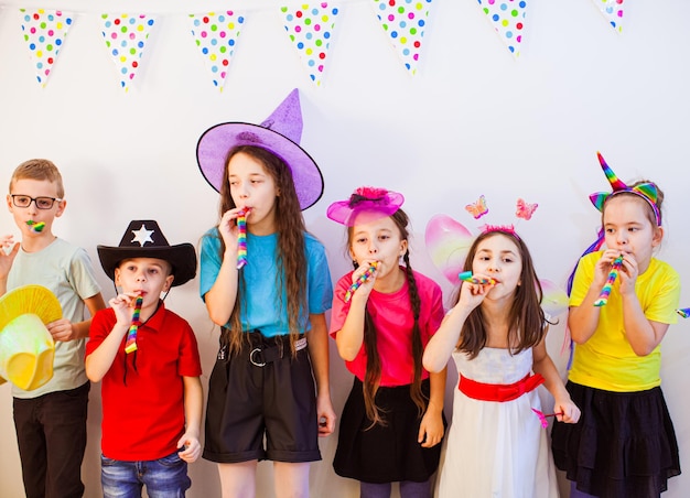 Celebração de aniversário com amigos Crianças usando chapéus engraçados Amigos felizes soprando apitos em uma festa de aniversário Conceito de amizade