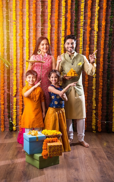 Celebração de Diwali ou Rakshabandhan - jovem família indiana de quatro pessoas celebrando o festival Deepavali ou bhai Dooj com doce laddoo, lâmpada a óleo ou diya e caixas de presente, comendo comida ou tomando selfie