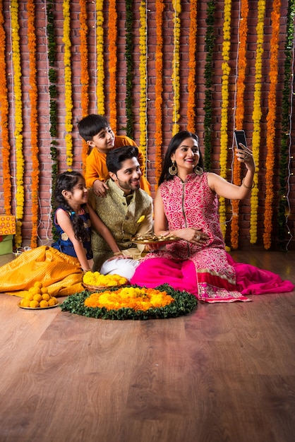 Celebração de Diwali ou Rakshabandhan - jovem família indiana de quatro pessoas celebrando o festival Deepavali ou bhai Dooj com doce laddoo, lâmpada a óleo ou diya e caixas de presente, comendo comida ou tomando selfie