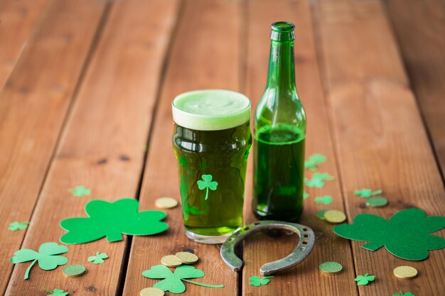 celebração de feriados e dia de São Patrício conceito copo de cerveja verde com garrafa de trevo ferradura e moedas de ouro em mesa de madeira