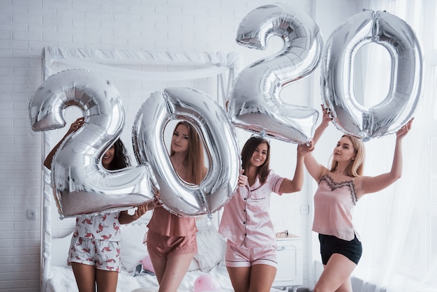 Celebração de férias. Quatro meninas em roupas rosa e brancas fica com balões prateados. Concepção de feliz ano novo