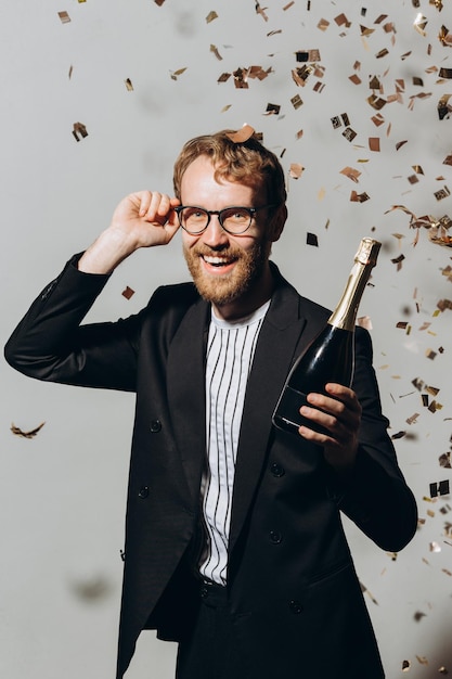Celebração do ano novo Jovem ruivo com uma garrafa de champanhe isolada em um fundo branco sob confete