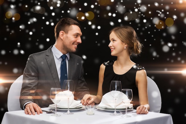 Celebração, natal, feriados e conceito de pessoas - casal sorridente no restaurante sobre fundo de luzes noturnas