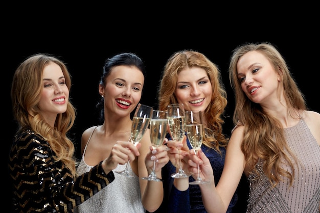 Foto celebración, amigos, despedida de soltera y concepto de vacaciones - mujeres felices tintineando copas de champán sobre fondo negro