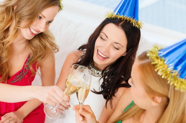 celebración, bebidas, amigos, despedida de soltera, concepto de cumpleaños - tres mujeres sonrientes con sombreros azules con copas de champán