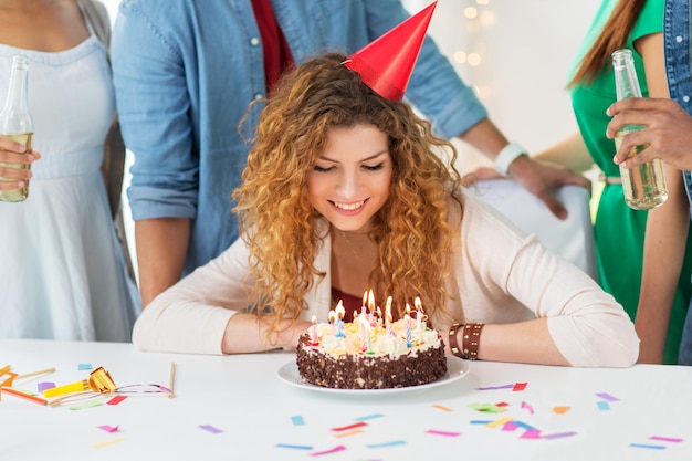 celebración y concepto de la gente - feliz mujer pelirroja sonriente con velas encendidas en el pastel de cumpleaños en la fiesta en casa