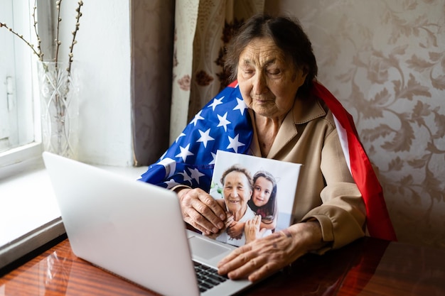 Celebración del Día de la Independencia después de la cuarentena. Granny mirando la pantalla de un portátil y celebrando la fiesta nacional con su familia en línea, se preocupa por las personas mayores, la tecnología personal, se centra en la mujer.