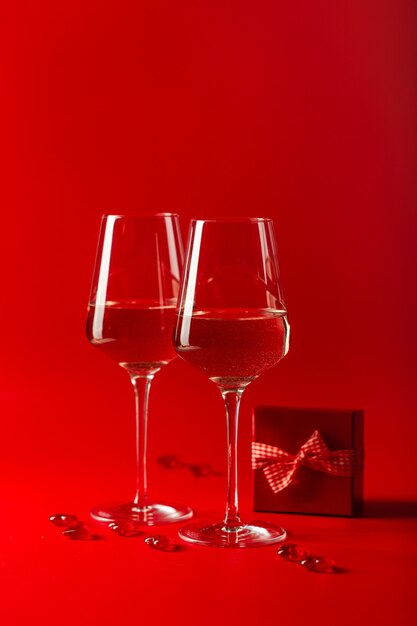 Celebración del día de san valentín. dos copas llenas de vino, corazones decorativos y caja de regalo roja