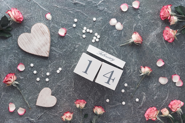Celebración del día de San Valentín, plano con calendario de madera, rosas rosadas y corazones de madera.