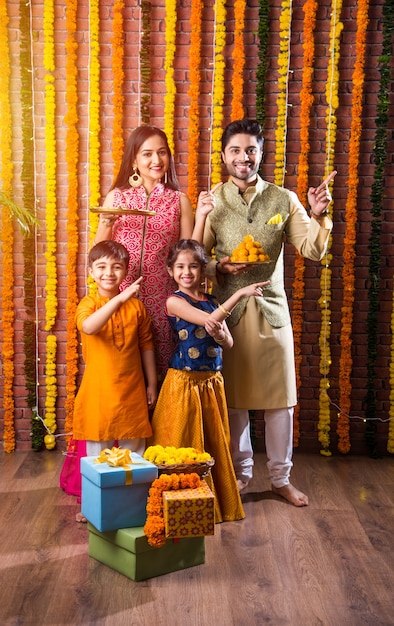 Foto celebración de diwali o rakshabandhan: joven familia india de cuatro miembros que celebra el festival deepavali o bhai dooj con laddoo dulce, lámpara de aceite o diya y cajas de regalo, comiendo o tomando selfie