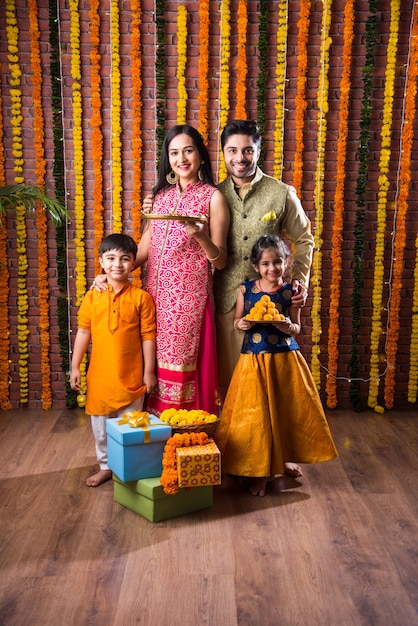 Celebración de Diwali o Rakshabandhan: joven familia india de cuatro miembros que celebra el festival Deepavali o bhai Dooj con laddoo dulce, lámpara de aceite o diya y cajas de regalo, comiendo o tomando selfie