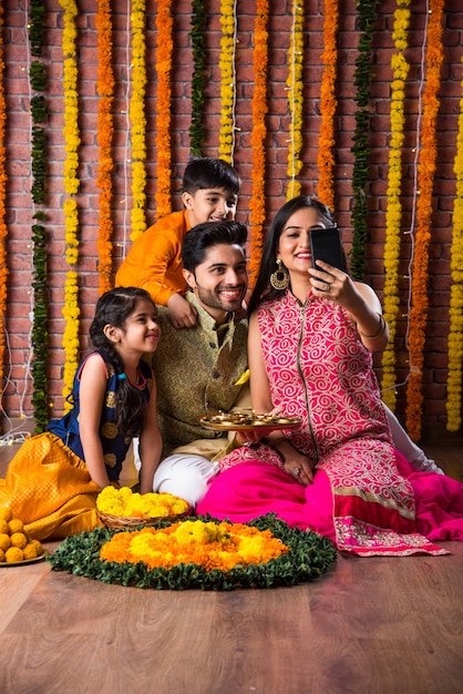 Celebración de Diwali o Rakshabandhan: joven familia india de cuatro miembros que celebra el festival Deepavali o bhai Dooj con laddoo dulce, lámpara de aceite o diya y cajas de regalo, comiendo o tomando selfie