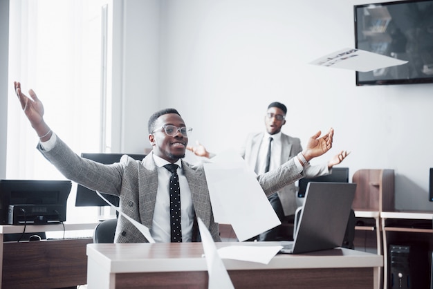 Celebración de dos guapo empresario afroamericano alegre exitoso con tirar papel en el lugar de trabajo