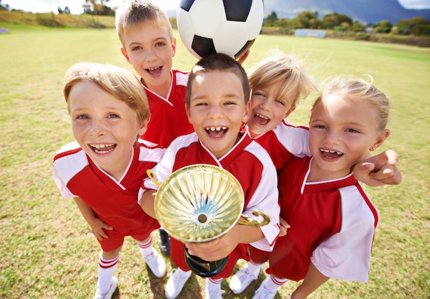 Foto celebración equipo de fútbol y niños con copa niños y niñas con apoyo de victoria o orgulloso logro deportivo y amistad juntos y feliz por ganar listo para el juego o la actividad física