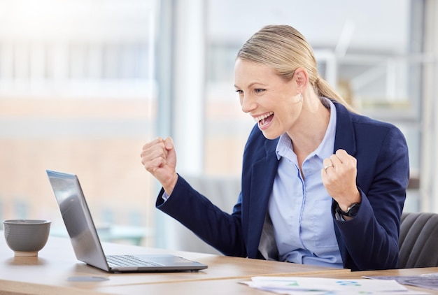 Celebración de éxito y mujer de negocios en una computadora portátil en su escritorio en la oficina corporativa moderna Feliz celebración y victoria del gerente profesional con una sonrisa y levantando el puño con felicidad y orgullo