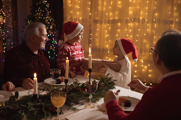 Celebración familiar de Navidad. Familia feliz disfrutando de la cena de Navidad en casa. Dos hermanos intercambiando cajas de regalo, presente para hermano.