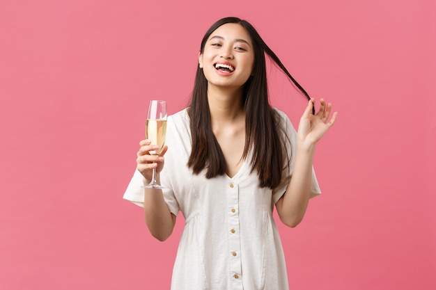 Celebración, fiestas y concepto de diversión. Mujer joven coqueta y coqueta con copa de champán tratando de seducir al chico en la celebración del evento, riendo y sonriendo tontamente sobre fondo rosa.