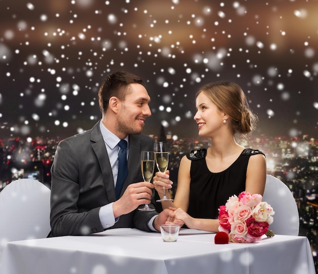 celebración, navidad, vacaciones y concepto de la gente - pareja sonriente tomando copas de vino espumoso en el restaurante sobre el fondo de la ciudad de noche nevada