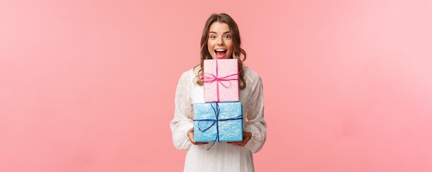 Celebración navideña y concepto de mujer Retrato de niña feliz y alegre le gusta celebrar cumpleaños y recibir regalos sosteniendo dos cajas de regalo y cámara sonriente fondo rosa