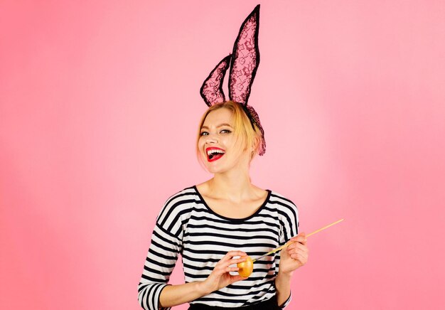 Celebración de pascua mujer sonriente en orejas de conejo pintando huevo con pincel huevos de colores primavera