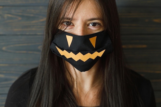 Foto celebración segura de halloween mujer joven con máscara negra malvada sobre fondo de madera oscura