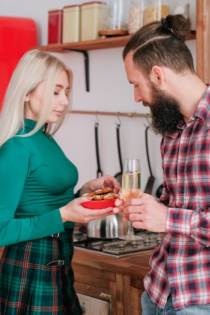 Celebración de las vacaciones de invierno en casa. Pareja bebiendo champán en la cocina. Lady hizo galletas de jengibre.