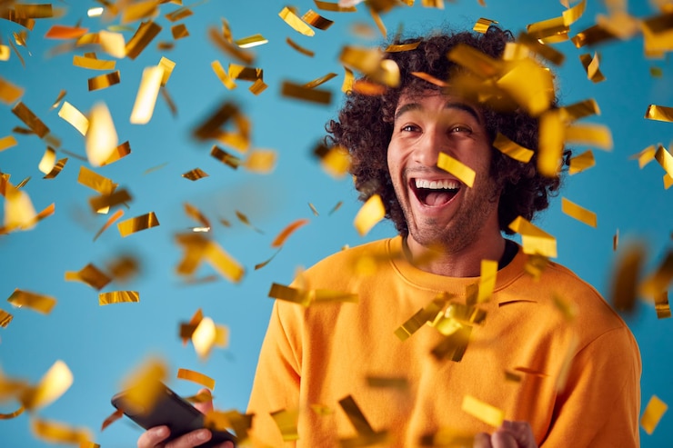 Foto celebran a un joven con un teléfono móvil ganando un premio y bañado con confeti dorado en el estudio